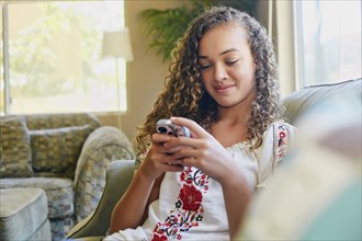 Mixed race girl using cell phone on sofa