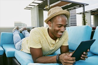 Black man using digital tablet on sofa on urban rooftop