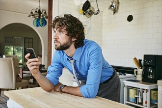 Caucasian businessman using cell phone in kitchen