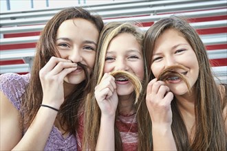 Teenage girls making fake mustaches with hair