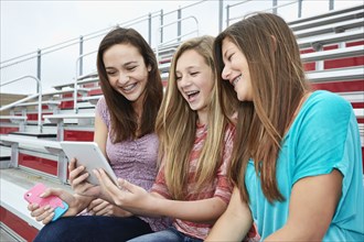 Teenage girls using digital tablet in bleachers