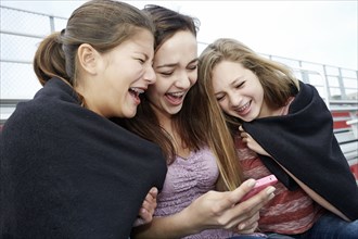 Teenage girls using cell phone in blanket