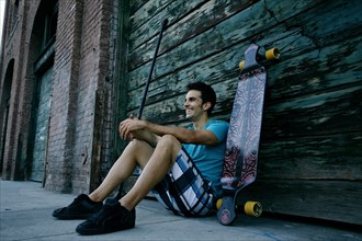 Caucasian man sitting with skateboard and land paddle