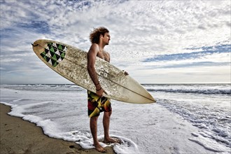 Caucasian man holding surfboard in waves on beach