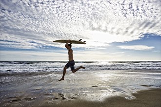 Caucasian man jumping with surfboard on beach