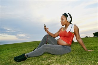 Pregnant woman listening to headphones in park