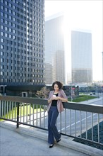 Mixed race businesswoman using cell phone on urban sky bridge