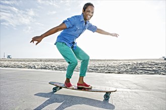Older Black woman skateboarding by beach