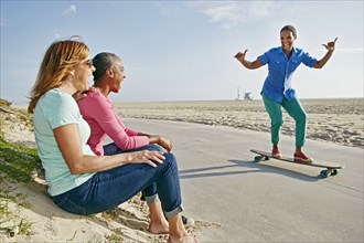 Older Black woman skateboarding by friends on beach