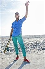 Older Black woman holding skateboard on beach