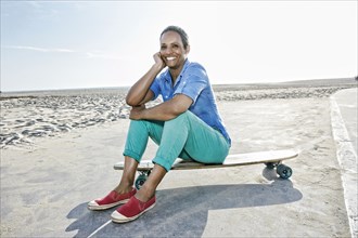 Older Black woman sitting on skateboard on beach