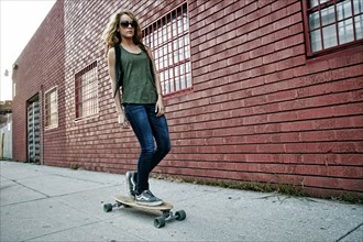 Mixed race woman riding skateboard on city street