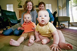 Caucasian mothers and babies sitting on living room floor