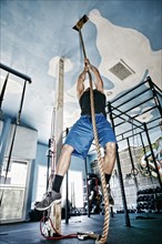African American man climbing rope in gym