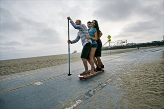 Friends skateboarding with paddle pole at beach