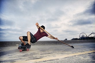 Caucasian man skateboarding with paddle pole at beach
