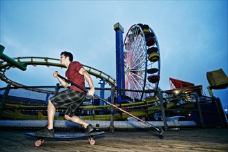 Caucasian man skateboarding with paddle pole at amusement park
