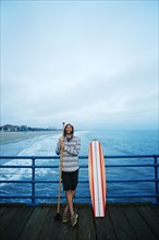 Caucasian man standing with skateboard and paddle pole on boardwalk