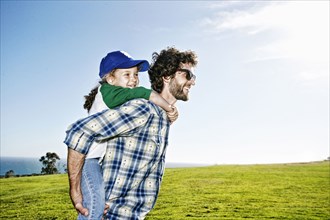 Father carrying daughter piggyback in grassy field