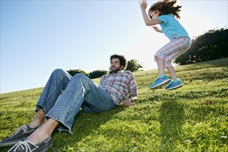 Girl jumping near father in grassy field