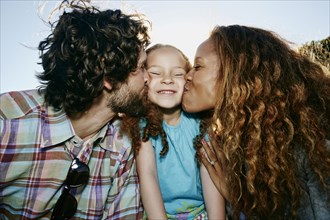 Parents kissing cheeks of daughter outdoors