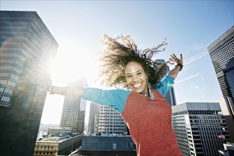 Mixed race woman cheering with arms outstretched on urban rooftop
