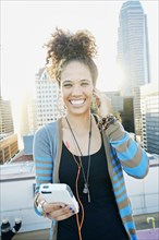 Mixed race woman listening to earbuds on urban rooftop