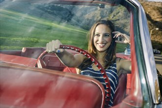 Hispanic woman driving in classic convertible