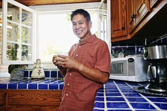 Filipino man drinking cup of coffee in kitchen