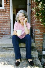 Caucasian woman drinking cup of coffee on front stoop