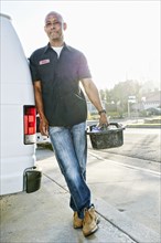 Mixed race plumber holding tools van