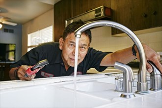 Pacific Islander plumber examining sink in kitchen