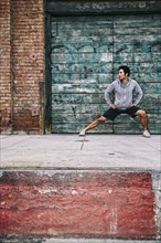 Mixed race man stretching near industrial building
