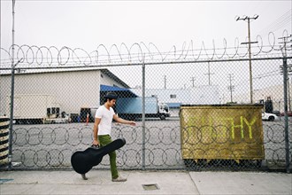 Mixed race musician carrying guitar case on sidewalk