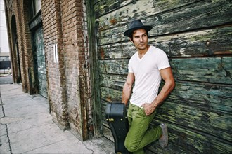Mixed race musician holding guitar case near industrial building