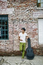 Mixed race musician with guitar case using cell phone