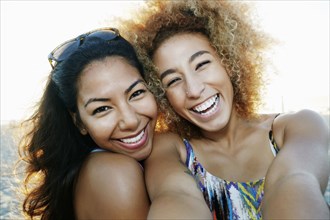 Smiling Hispanic women taking selfie together outdoors