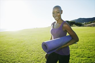 African American woman carrying yoga mat in park