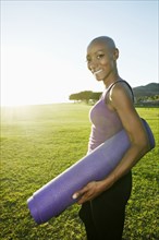 African American woman carrying yoga mat in park