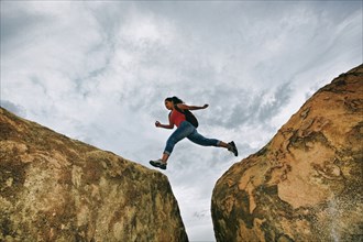 Hispanic woman jumping crevasse on rock formations
