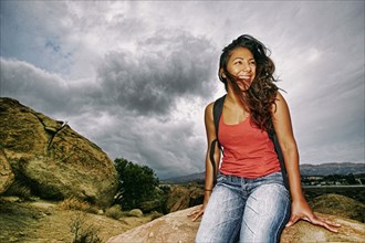 Hispanic woman sitting on rocky hilltop