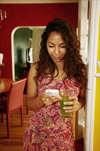 Hispanic woman drinking green juice and using cell phone