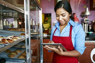 Hispanic waitress taking inventory with digital tablet in bakery