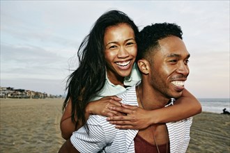 Man carrying girlfriend piggyback on beach