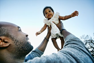 Black father holding baby daughter under blue sky