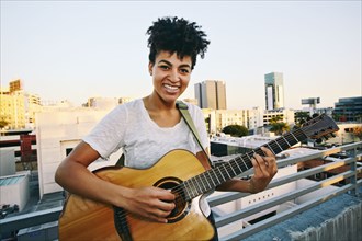 Smiling woman playing guitar on urban rooftop