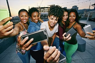 Women taking selfies with cell phones on urban rooftop