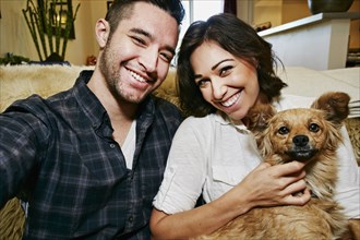 Couple holding dog on sofa in living room