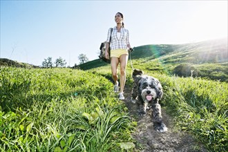 Mixed race woman walking dog on grassy hillside