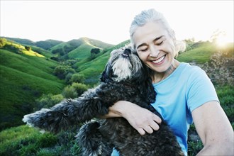 Older Caucasian woman hugging dog on rural hilltop